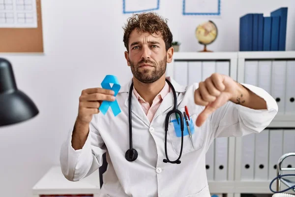 Joven Médico Hispano Sosteniendo Cinta Azul Con Cara Enojada Signo —  Fotos de Stock