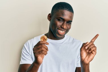 Genç Afrikalı Amerikalı adam sanal para birimi Bitcoin 'i tutuyor mutlu bir şekilde gülümsüyor. 
