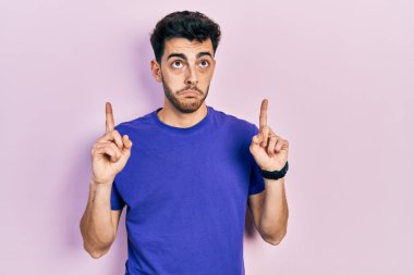 Gündelik tişört giyen genç İspanyol adam üzgün ve üzgün görünüyor, parmaklarıyla yönü gösteriyor, mutsuz ve depresif.. 