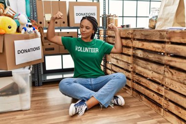 Bağışlarda gönüllü tişört giyen Afro-Amerikalı genç bir kadın kol kaslarının gururla gülümsediğini gösteriyor. fitness konsepti. 