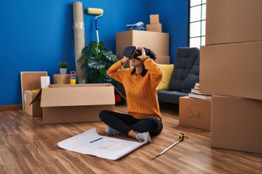 Genç Latin kadın yeni evinde sanal gerçeklik gözlüğü takarak kendine güveniyor.