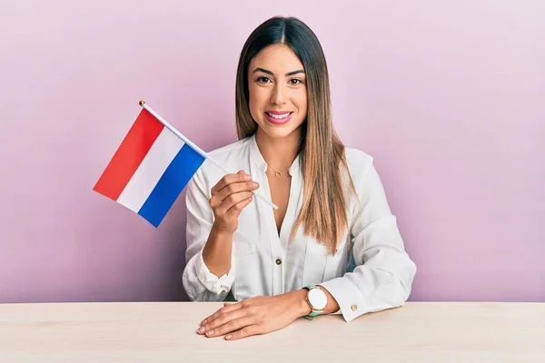 Ung Latinamerikansk Kvinna Håller Holland Flagga Sitter Bordet Ser Positiv — Stockfoto