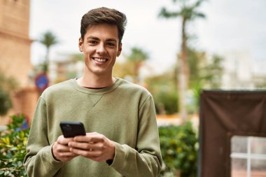 Genç İspanyol adam şehirde akıllı telefon kullanarak mutlu gülümsüyor..
