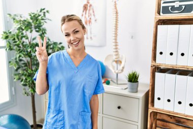 Ağrı kesici kliniğinde çalışan beyaz bir kadın kameraya gülümseyen bir gülümsemeyle zafer işareti yapıyor. İki numara.. 