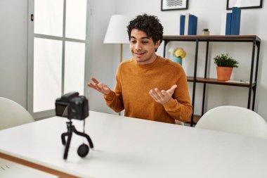 Evdeki kanepede oturan Latin asıllı genç bir adam kamerayla görüntülü görüşme yapıyor..