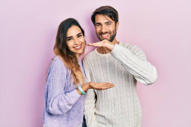 Latin kökenli genç bir çift, sıradan kıyafetler giyip büyük ve büyük boy işaretleri gösteriyorlar. Ölçü sembolü. Kameraya bakıp gülümsüyor. ölçüm kavramı. 