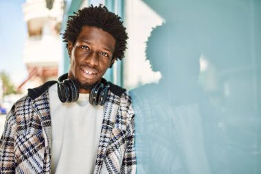 Afro saçlı, kulaklık takan yakışıklı, açık havada mutlu gülümseyen bir zenci.