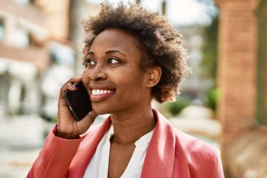 Güzel iş kadını afro saçlı Afro-Amerikan kadın mutlu ve kendinden emin bir şekilde şehirde telefonda konuşuyor.