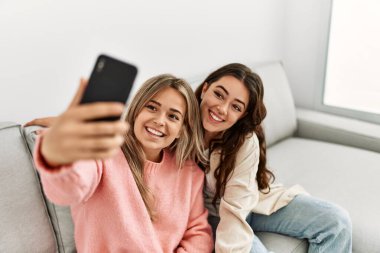 Genç çift mutlu bir şekilde gülümsüyor. Evdeki akıllı telefonun yanında selfie çekiyorlar..