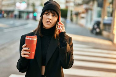 Genç İspanyol kadın akıllı telefondan konuşuyor ve şehirde kahve içiyor..