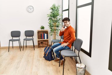 Young hispanic man smiling confident talking on the smartphone at waiting room