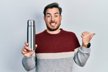Sakallı yakışıklı, beyaz bir adam. Termo tutuyor. Parmağını yana doğru uzatıp gülümsüyor. 