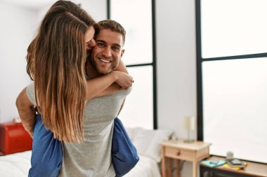 Genç beyaz bir adam yatak odasında kadını sırtında tutuyor..