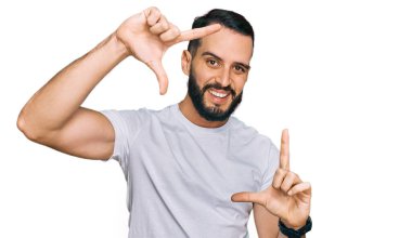 Sakallı, sıradan beyaz tişörtlü, gülümseyen, elleri ve parmakları gülen yüzlü genç bir adam. yaratıcılık ve fotoğrafçılık kavramı. 