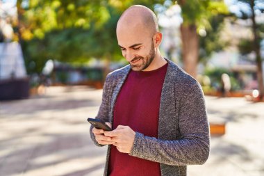 Genç adam parkta akıllı telefon kullanarak kendinden emin gülümsüyor.