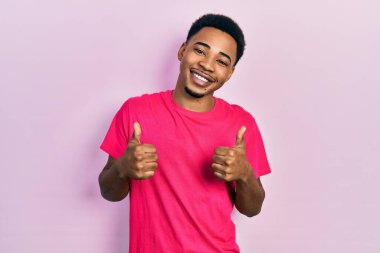 Genç Afrikalı Amerikalı adam Casua t-shirt 'ü giyiyor. Başarı işareti el hareketleriyle olumlu jest yapıyor. Gülümsüyor ve mutlu. Neşeli ifade ve kazanan jest. 