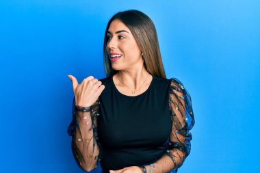 Gündelik kıyafetler giyen, gülen yüzlü genç İspanyol kadın başparmağıyla yan tarafa bakıyor ve işaret ediyor.. 