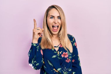 Gündelik giysiler giyen genç beyaz kadın başarılı bir fikirle işaret ediyor. Heyecanlı ve mutlu. Bir numara.. 