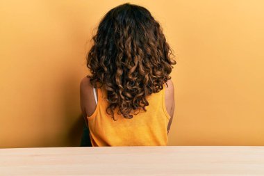 Orta yaşlı, güzel bir kadın, gündelik giysiler giyip masanın üzerinde oturur arkasını kollarını kavuşturup başka tarafa bakar. 