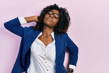 Genç Afrikalı Amerikalı kadın iş kıyafetleri ve gözlük takıyor boyun ağrısı çekiyor, boynuna elle dokunuyor, kas ağrısı çekiyor. 