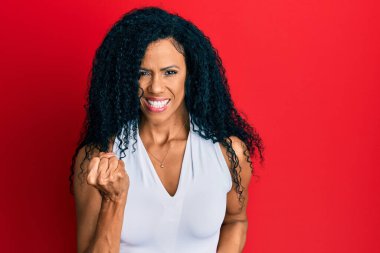 Orta yaşlı Afro-Amerikalı kadın, gündelik beyaz tişört giyip şaşkınlık ve şaşkınlık içinde, kolları havada ve gözleri kapalı bir şekilde başarıyı kutluyor. 