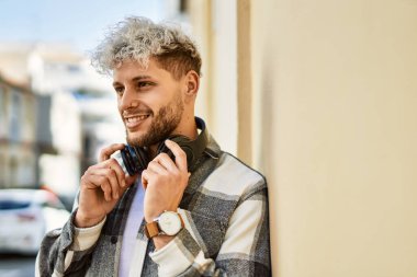 Şehirde kulaklık takarak mutlu gülümseyen genç İspanyol adam..