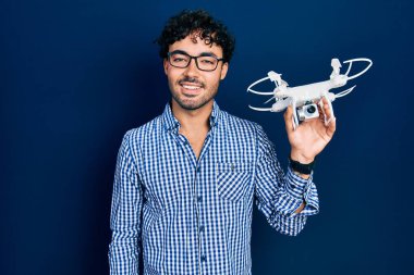 İHA 'yı tutan genç İspanyol adam pozitif ve mutlu görünüyor. Duruyor ve gülümsüyor. Kendine güvenen bir gülümsemeyle dişlerini gösteriyor. 