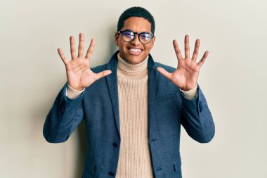 Zarif kıyafetler ve gözlük takan yakışıklı İspanyol adam on numarayı gösterip işaret ederken kendinden emin ve mutlu bir şekilde gülümsüyor.. 