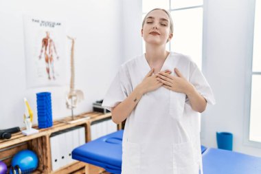 Ağrı kesici kliniğinde çalışan beyaz bir kadın elleri göğsünde, gözleri kapalı ve yüzünde minnet dolu bir jest ile gülümsüyor. sağlık kavramı. 