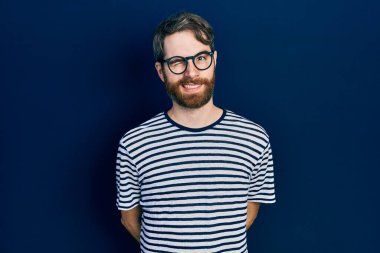 Sakallı, çizgili tişörtlü ve gözlüklü beyaz bir adam kameraya seksi bir ifadeyle bakıyor, neşeli ve mutlu bir yüzü var.. 