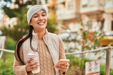 Genç Latin kadın şehirde kahve içerken akıllı telefon kullanıyor..