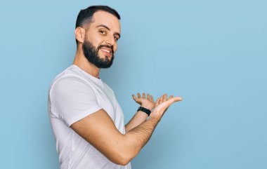 Sakallı, günlük beyaz tişörtlü genç adam gülümseyerek içeri girmeye davet ediyor. 