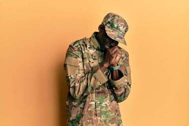 Asker üniforması giyen genç Afro-Amerikan adam elleri çenesinde gergin ve heyecanlı bir şekilde yan tarafa bakıyor. 