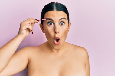Güzel esmer kadın kaşlarını fırçayla fırçalıyor. Korkmuş ve ağzı açık kalmış, şaşırmış. İnanmayan yüz. 