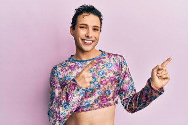 Makyaj elbisesi giymiş yakışıklı bir adam. Gülümsüyor ve kameraya bakıyor. İki eliyle ve parmaklarıyla onu işaret ediyor.. 