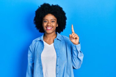 Genç Afro-Amerikalı kadın günlük giysiler giyip bir numaralı parmağını gösterirken kendine güvenen ve mutlu bir şekilde gülümsedi.. 