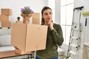 Genç İspanyol kadın elinde karton kutuyla ciddi bir yüzle hareket ederken eli çenesinde soru sorarken kafa karıştırıcı bir fikir hakkında düşünceli. 