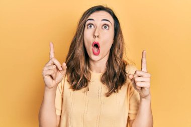 Gündelik kıyafetler giyen genç İspanyol kız şaşkın şaşkın yukarı bakıyor ve parmaklarıyla işaret ediyor ve kollarını kaldırıyor.. 