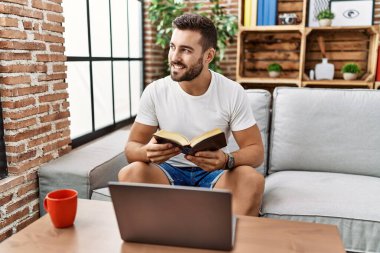 Genç İspanyol adam gülümsüyor evde kendinden emin bir şekilde kitap okuyor.