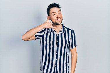 Günlük kıyafetler giymiş, gülümseyen genç İspanyol adam telefonla el ve parmak hareketleri yapıyor telefonda konuşur gibi. iletişim kavramları. 