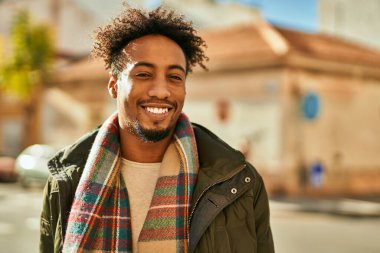 Genç Afrikalı Amerikalı adam gülümseyerek şehirde mutlu mesut duruyor.