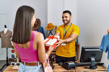 Genç Latin esnaf gülümseyerek giyim mağazasındaki müşteriye hediye veriyor..