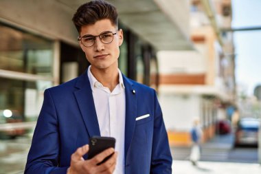 Sokakta takım elbise ve gözlük takan akıllı telefon kullanan genç adam.
