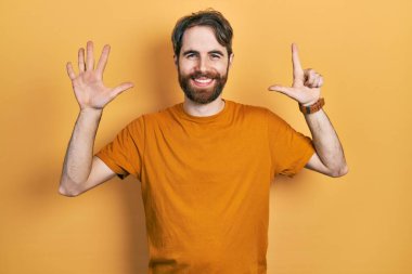 Sakallı, günlük sarı tişörtlü, beyaz bir adam 7 numarayı gösteriyor ve gülümsüyor. Kendinden emin ve mutlu.. 