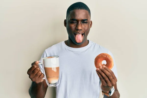 Νεαρός Αφροαμερικάνος Τρώει Ντόνατ Και Πίνει Καφέ Βγάζοντας Γλώσσα Του — Φωτογραφία Αρχείου