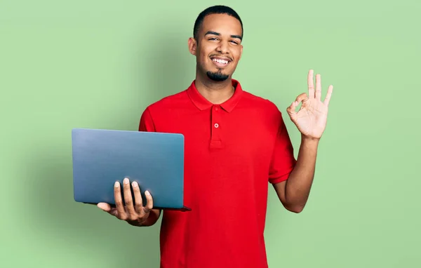 若いアフリカ系アメリカ人の男は指でOkサインを行うコンピュータのラップトップを使用して作業し 優しいジェスチャー優れたシンボルを笑顔 — ストック写真