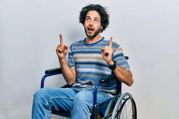 Handsome Hispanic Man Sitting Wheelchair Amazed Surprised Looking Pointing Fingers — Stock Photo, Image