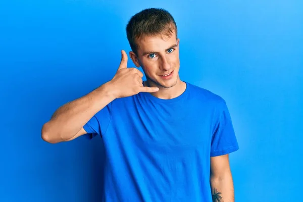 年轻的高加索人穿着休闲的蓝色T恤 微笑着用手和手指做电话手势 就像在电话里说话一样 交流概念 — 图库照片