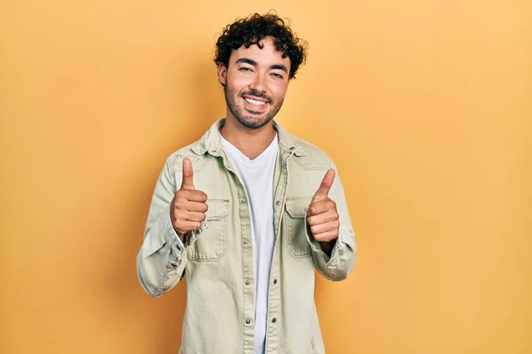 若いヒスパニック系の男性が手で積極的なジェスチャーを行うカジュアルな服の成功サインを着て 親指を笑顔と幸せ 陽気な表情と勝者のジェスチャー — ストック写真