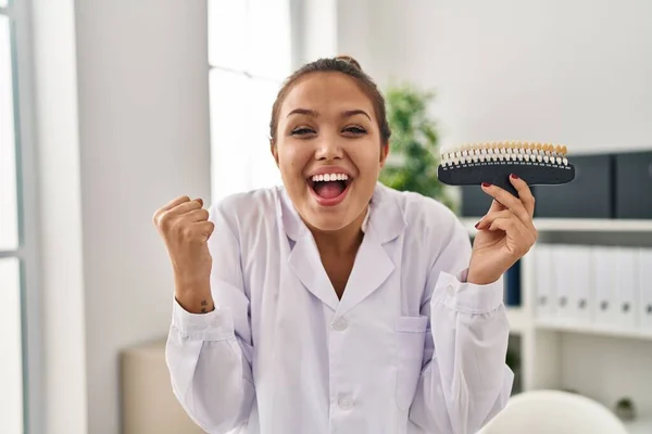 歯のホワイトニングのサンプルを保持している若いヒスパニック系の歯科医の女性は誇りに思って叫んで 勝利と成功を祝う非常に腕を上げ興奮 — ストック写真